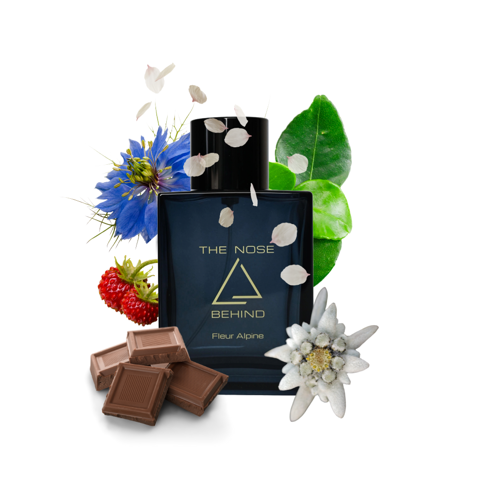 Parfümflakon „Fleur Alpine“ von „The Nose Behind“ umgeben von natürlichen Duftnoten: blauer Blüte, Edelweiß, grünen Blättern, Erdbeere, Schokoladenstücken und herabfallenden Blütenblättern. Die Bildkomposition symbolisiert die Duftkomponenten des Parfüms – floral, fruchtig und gourmand.